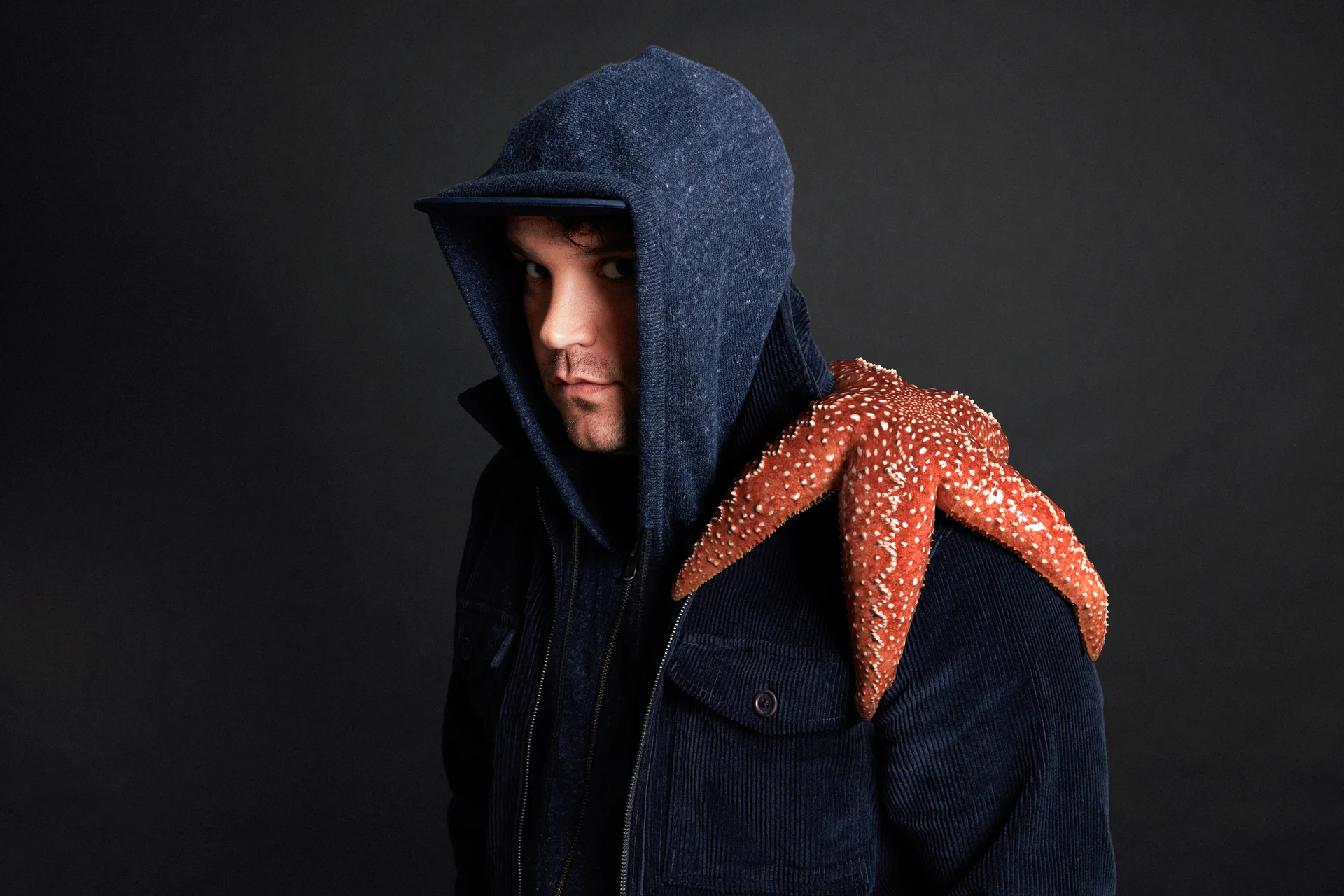 Man in a hooded jacket with a red starfish on his shoulder, low-key lighting portrait
